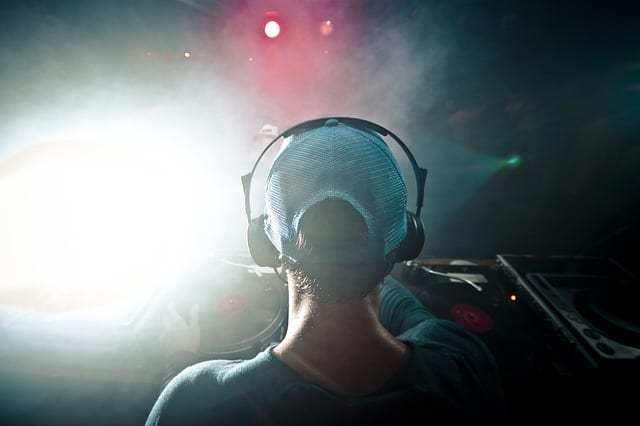 A male DJ wears headphones, and his audience is in front of him