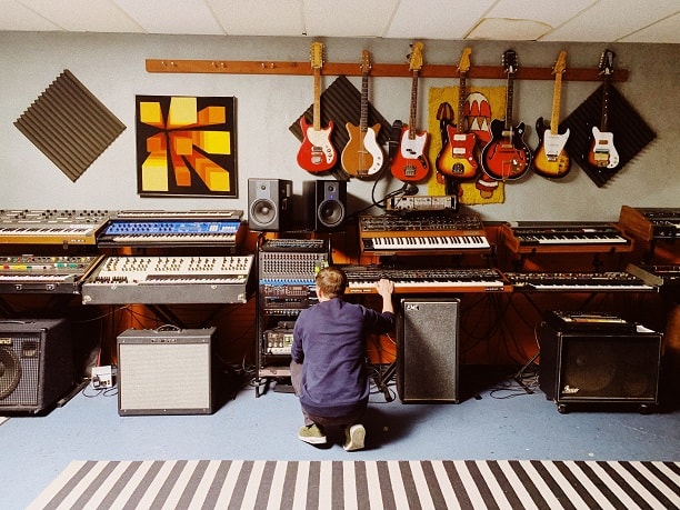 A man touching a synthesizer in a place with more music equipment
